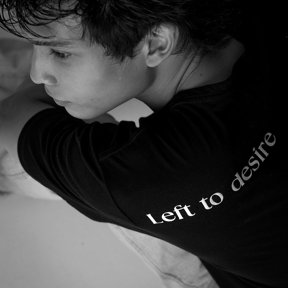 Person wearing a black shirt with 'Left to desire' text, sitting.