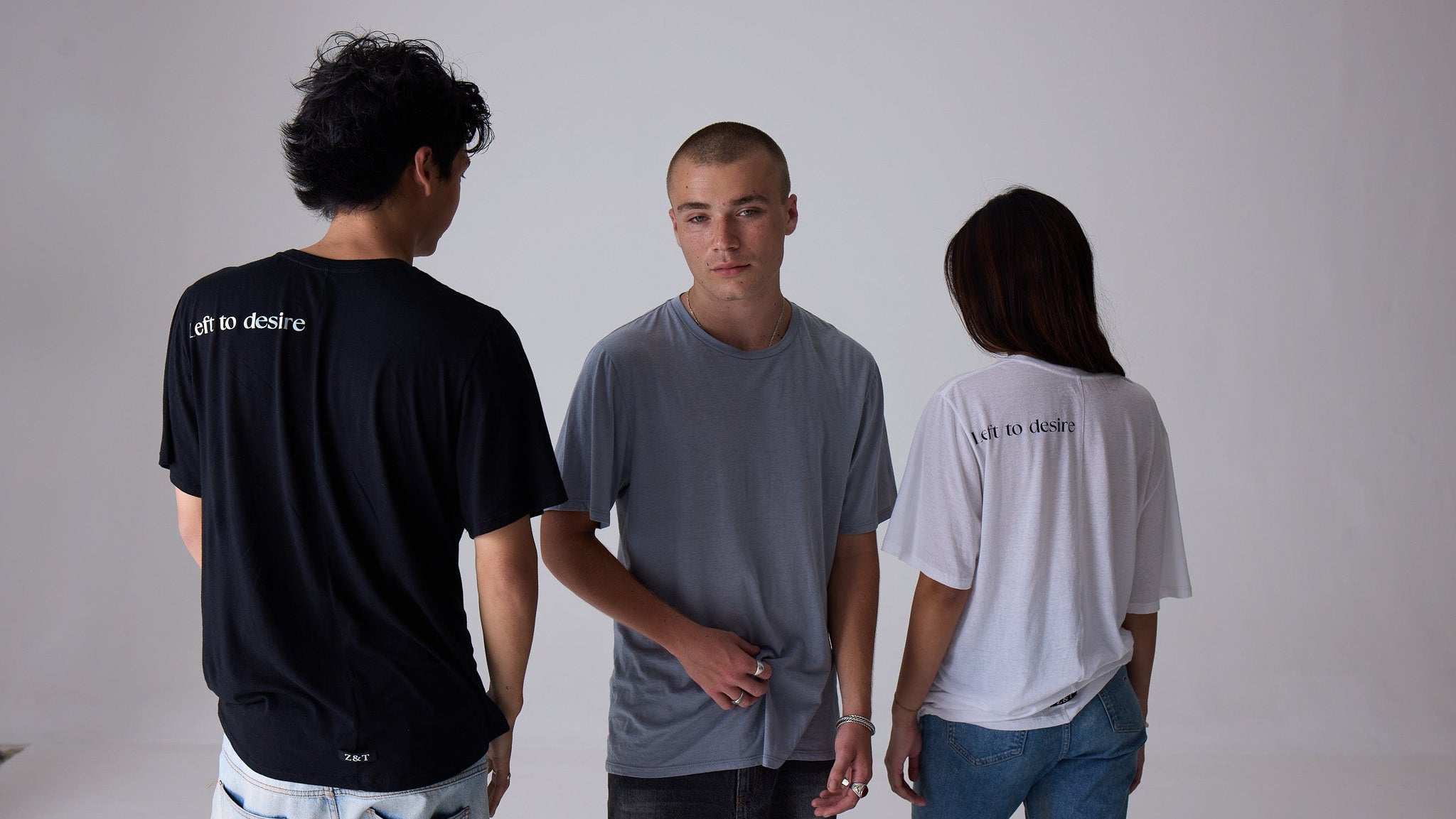 Three people wearing t-shirts with text on a plain background